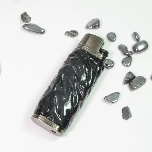 Textured black lighter case with metallic accents, surrounded by polished stones, Mellow Sora.